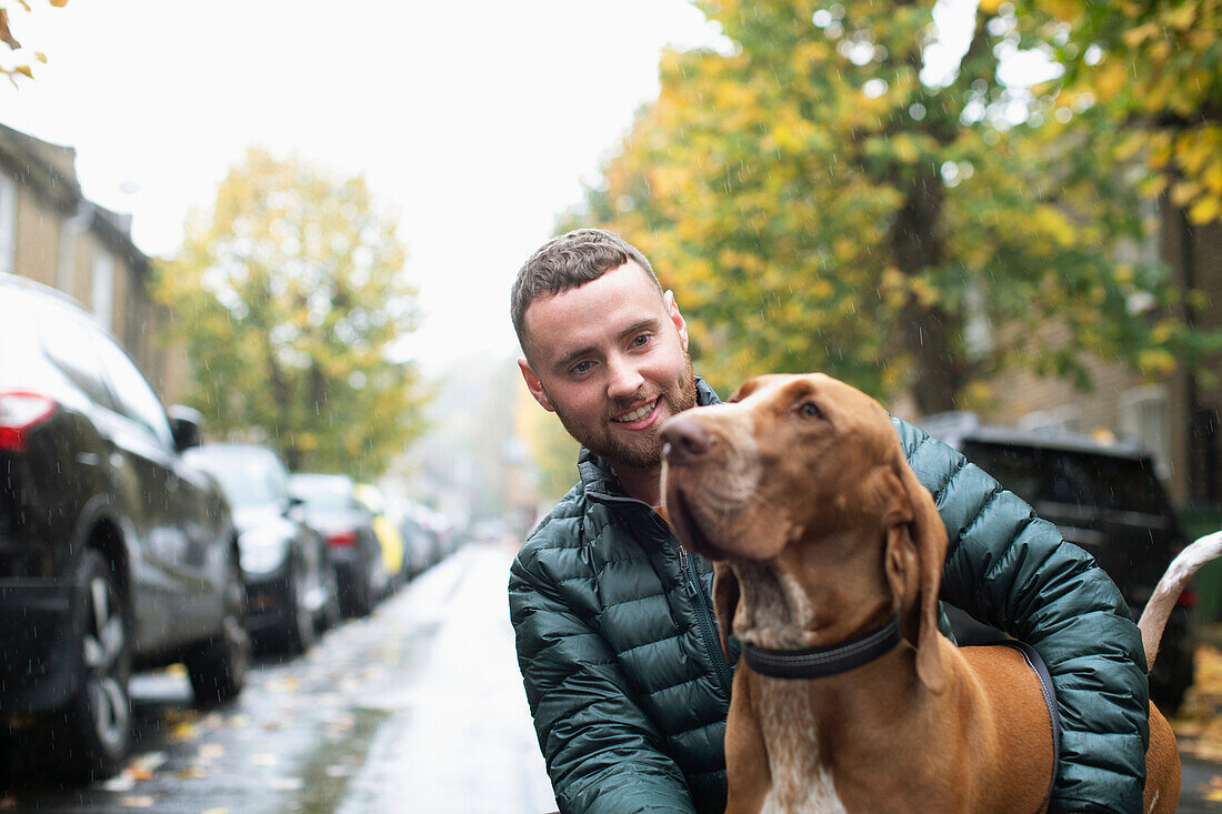 Happy young man with dog on wet urban street
