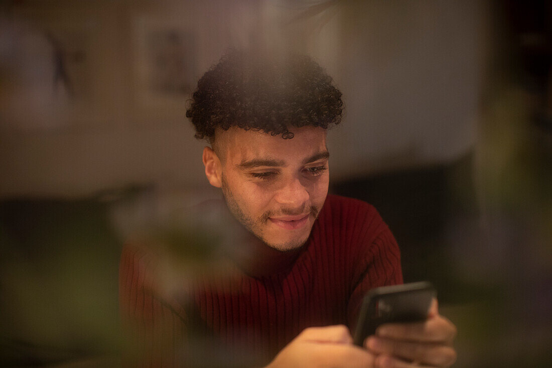 Smiling young man using smart phone in window