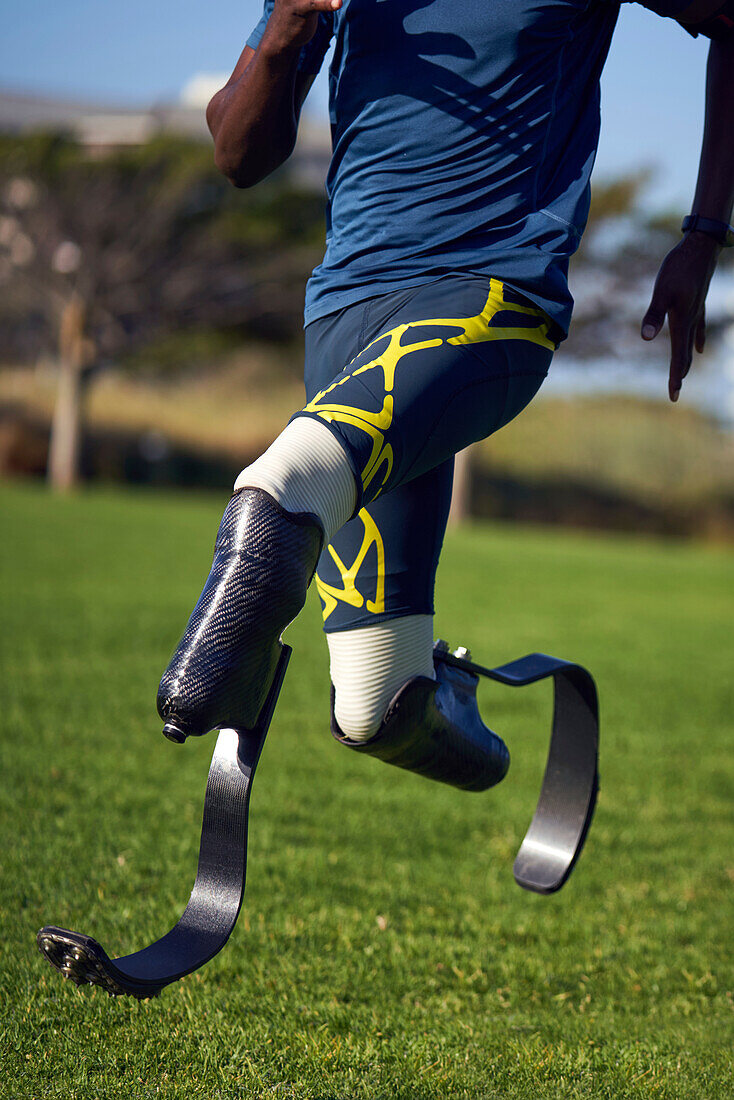 Male amputee athlete sprinting on sunny grass