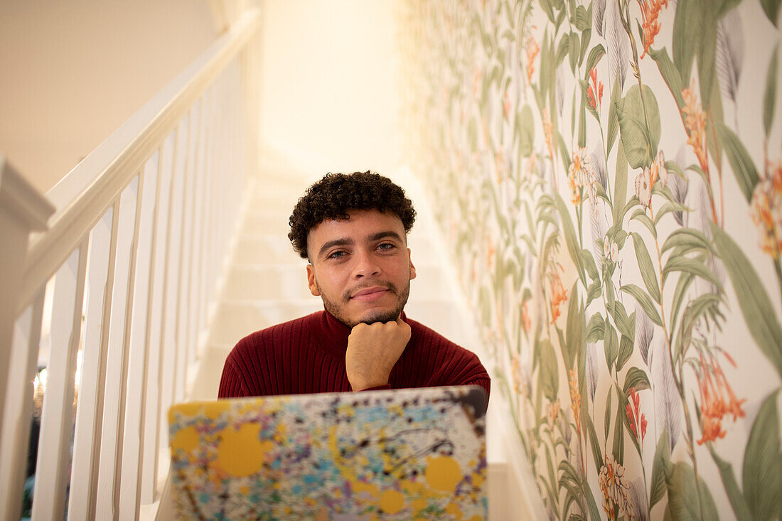 Confident young man with laptop on staircase at home