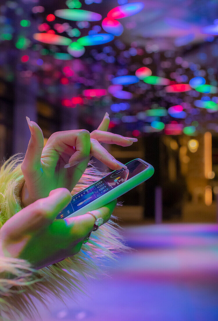 Woman using smart phone in nightclub under neon lights