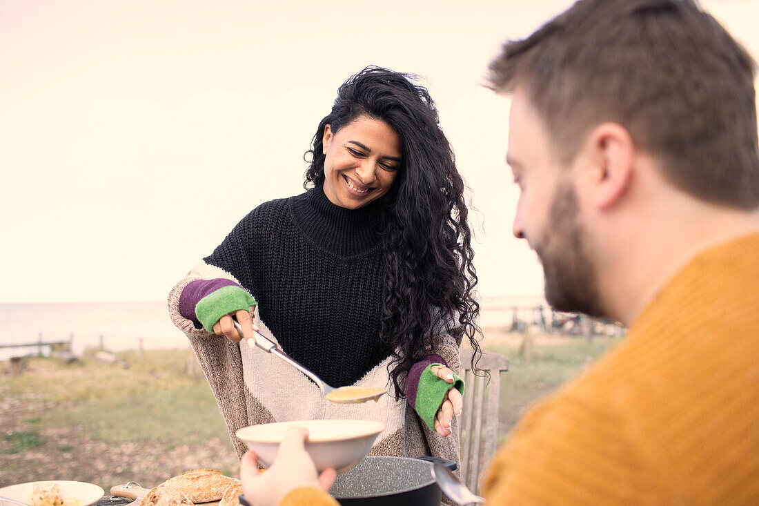 Happy woman serving chowder to boyfriend on beach patio