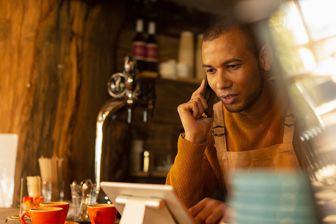 Male cafe owner taking order by phone at digital tablet