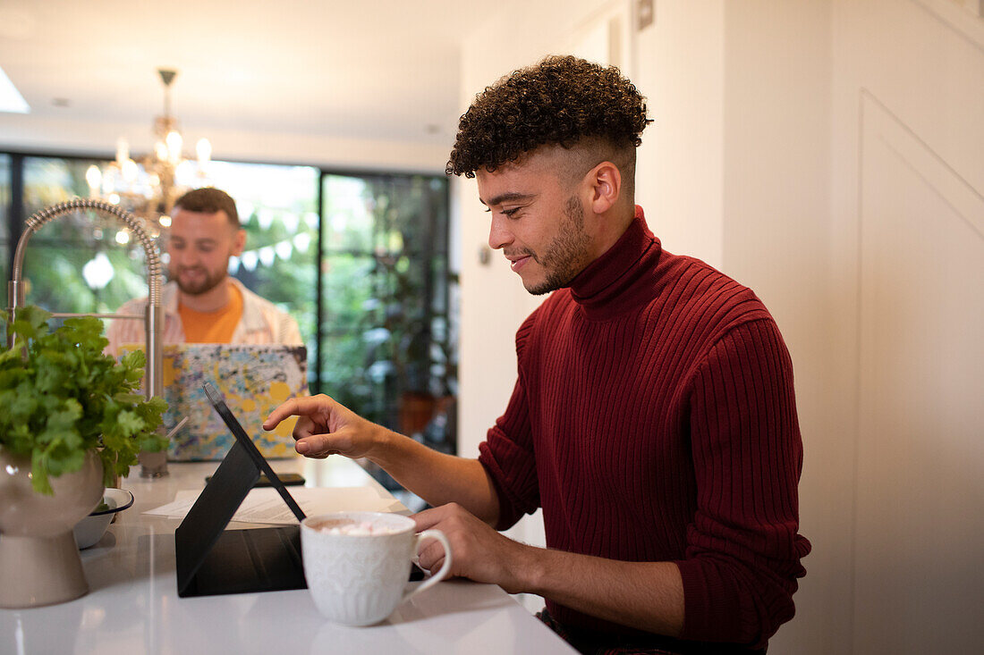 Young man working from home at digital tablet in kitchen