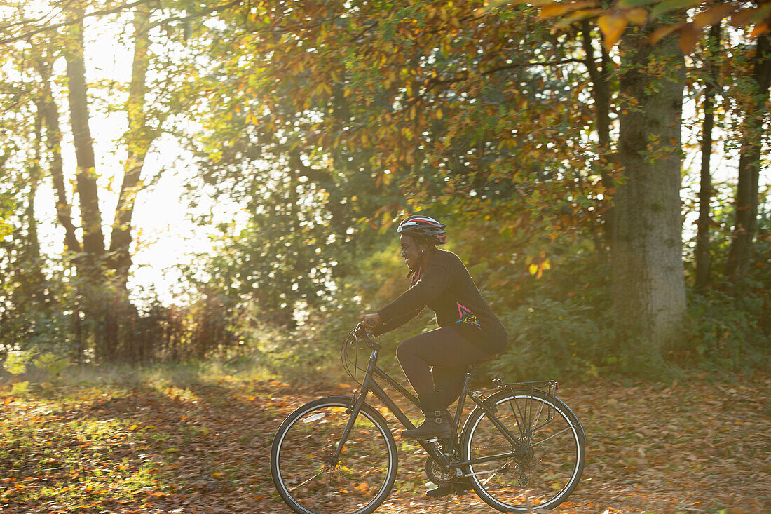 Happy woman bike riding among autumn leaves in sunny park