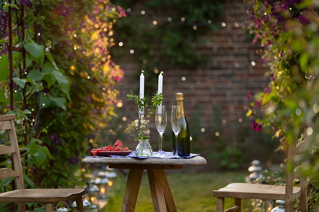 Champagne and red currants on table with candles in garden