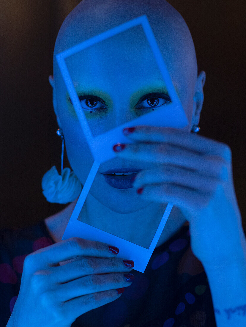 Woman with shaved head holding polaroids