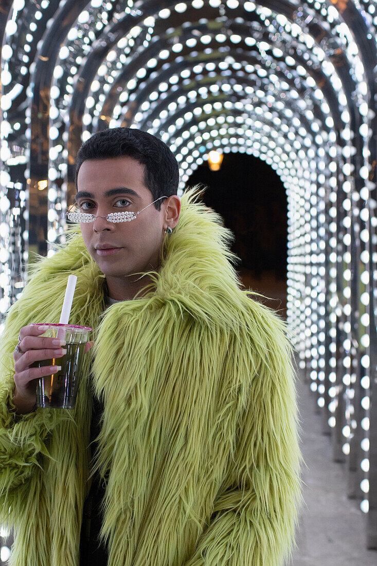 Young man in green fur coat under arch lights