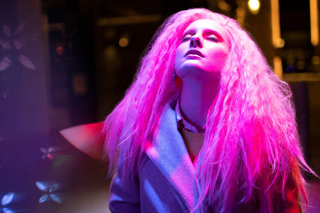 Woman with pink hair and head back under light