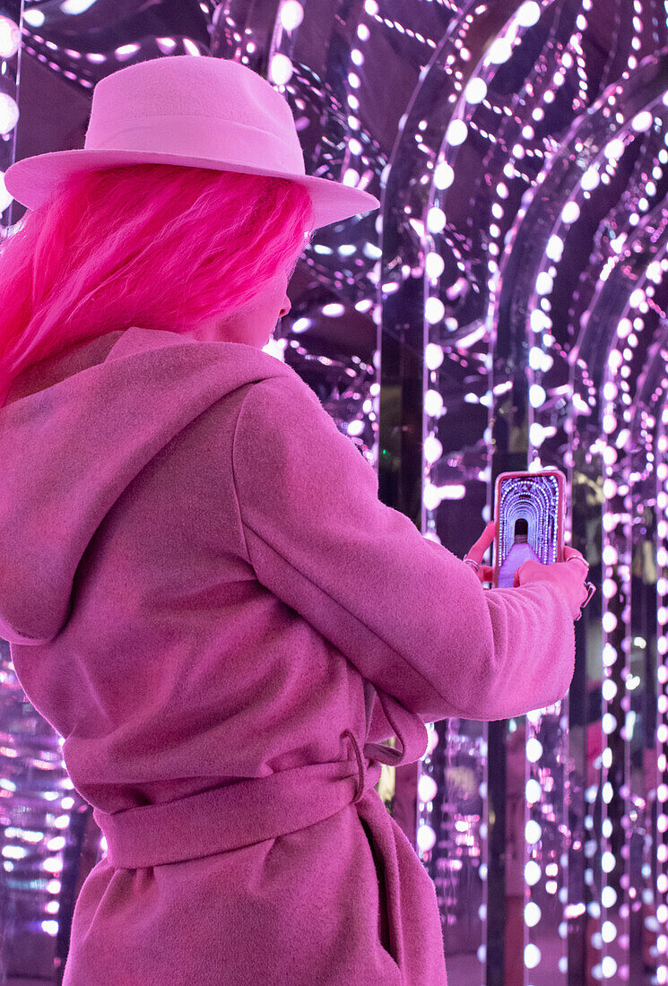 Woman in pink coat using camera phone under lights