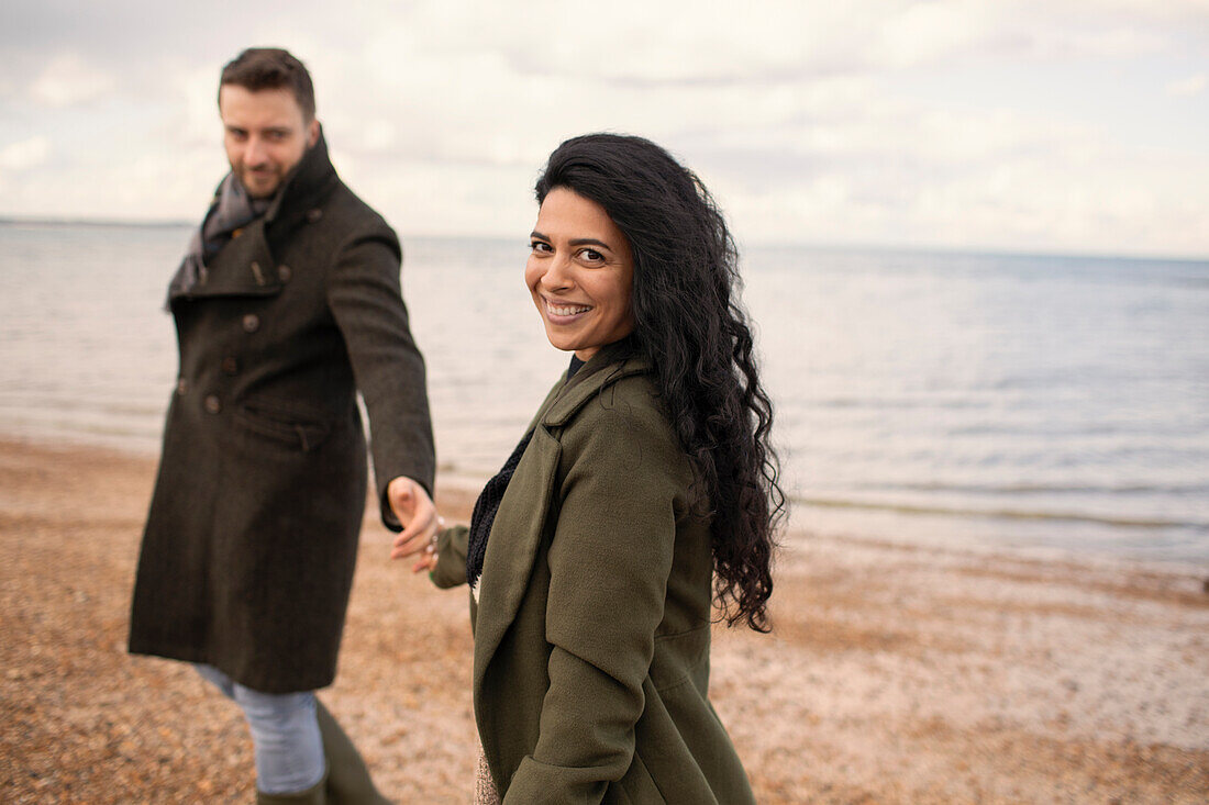 Happy couple in winter coats holding hands on beach