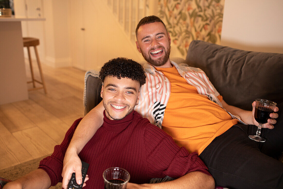 Happy gay male couple drinking wine on sofa at home