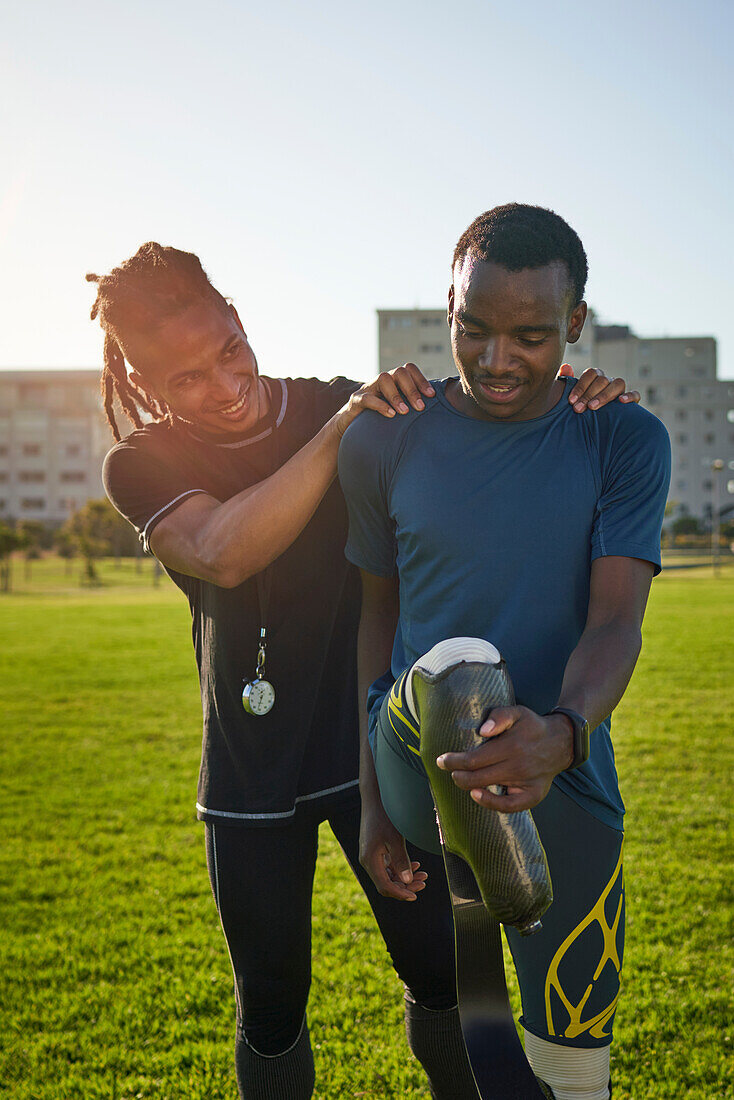 Coach supporting young amputee athlete stretching in park