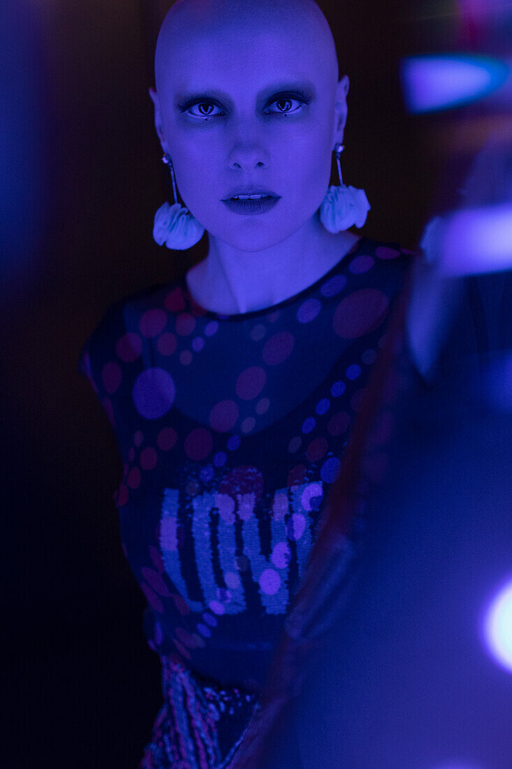 Serious woman with shaved head in dark neon blue light
