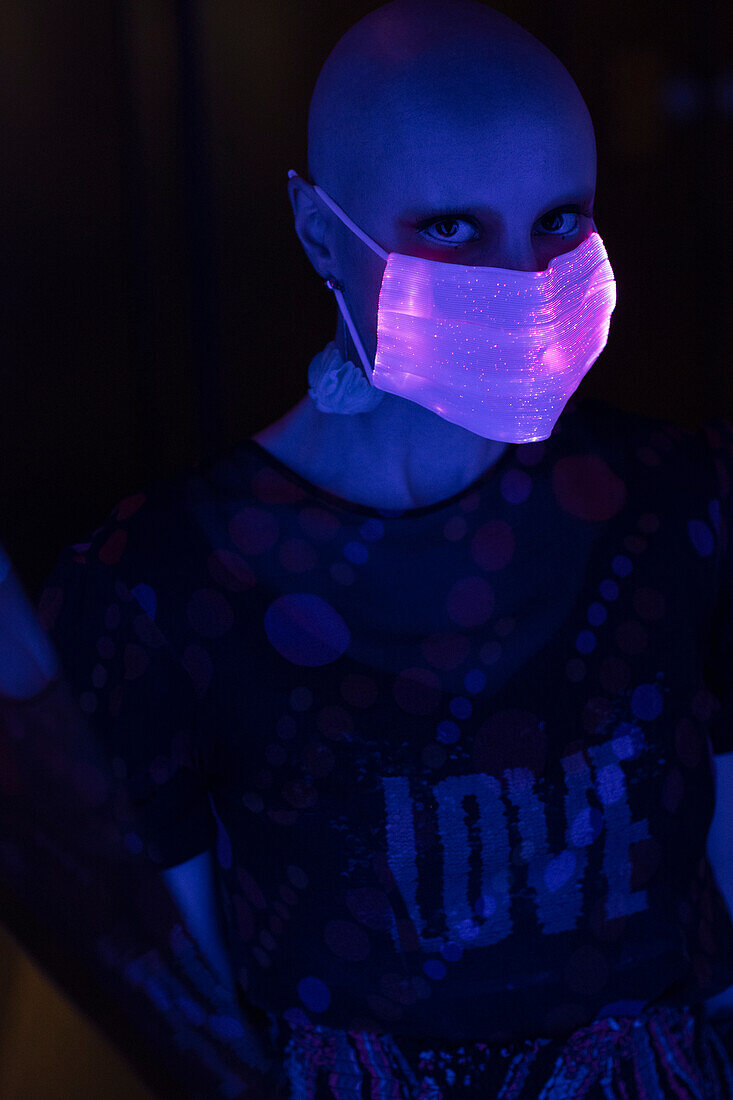Woman with shaved head in iridescent face mask in dark