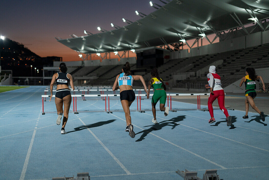 Female athletes racing toward hurdles in stadium