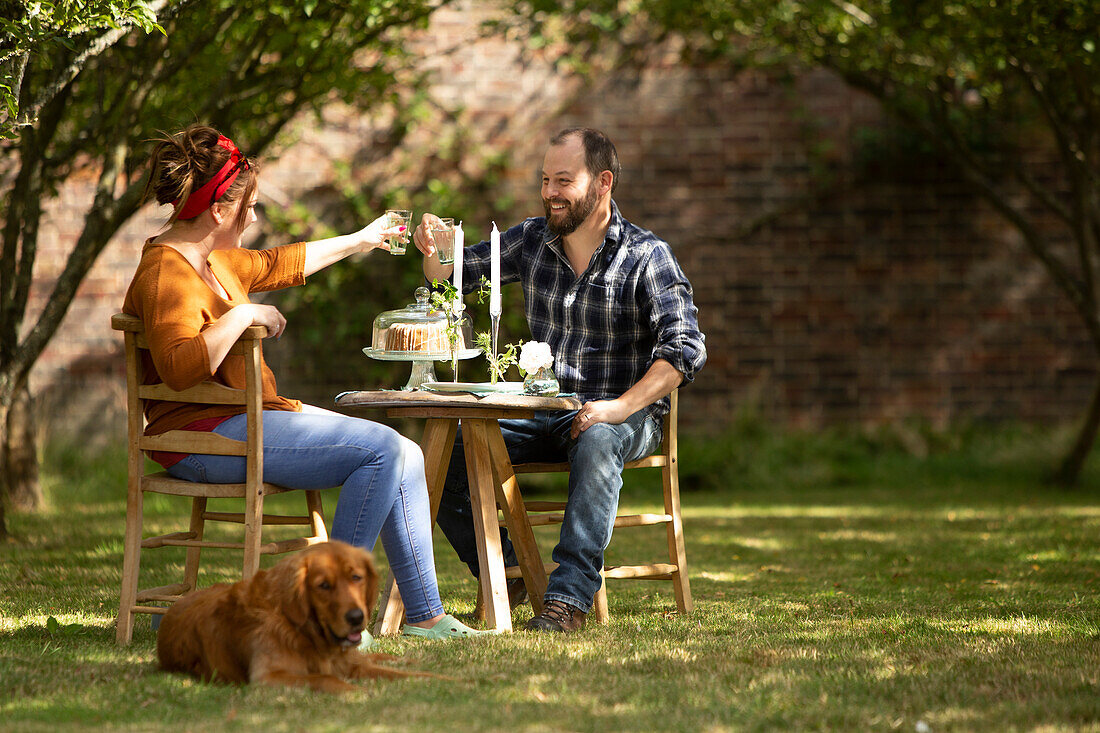 Happy couple with dog toasting glasses at table in garden