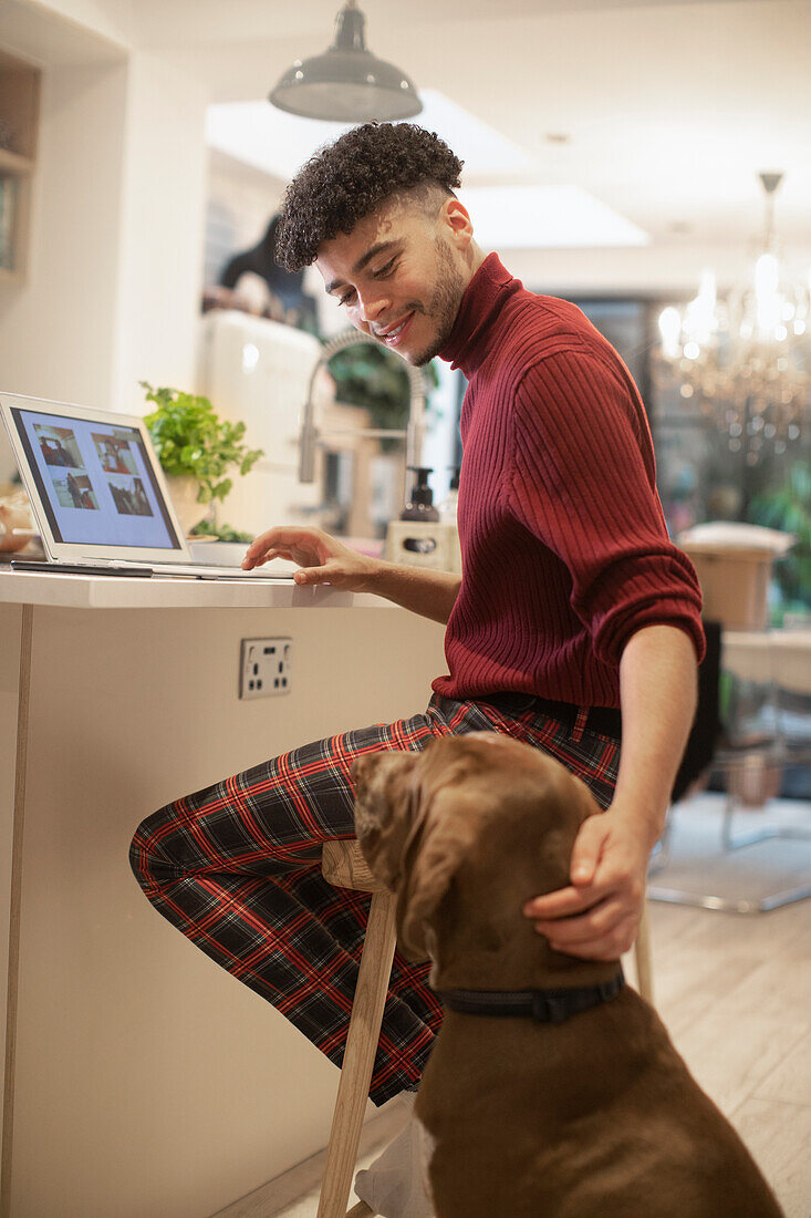 Young man working from home on laptop and petting dog
