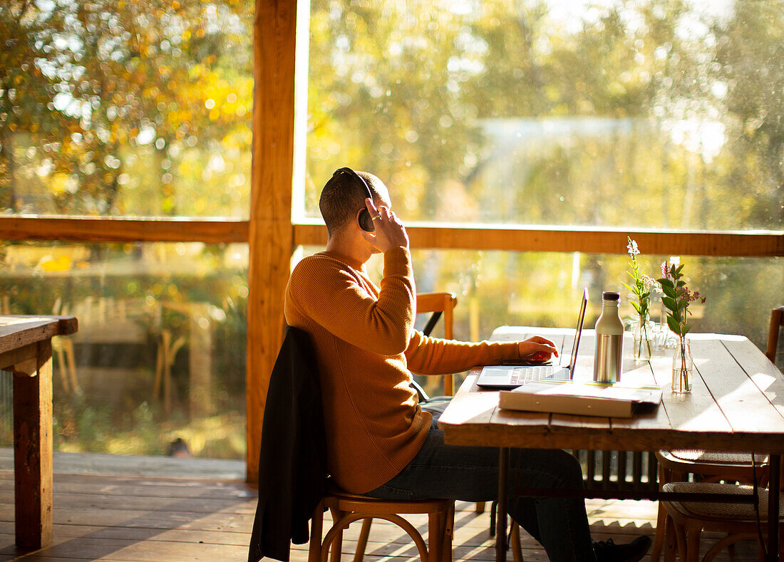 Businessman with headphones working on laptop in cafe