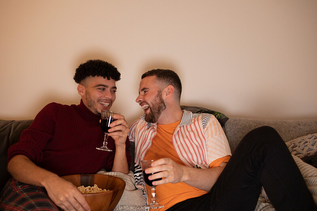 Happy gay couple drinking red wine and eating popcorn