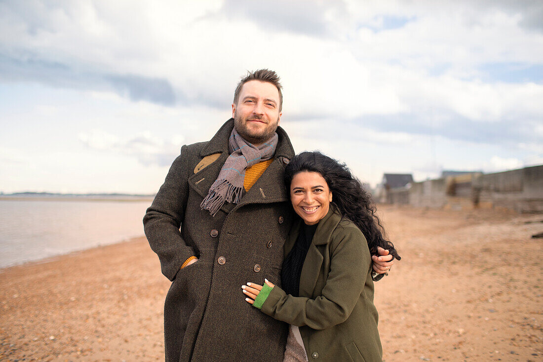 Happy affectionate couple in winter coats hugging on beach