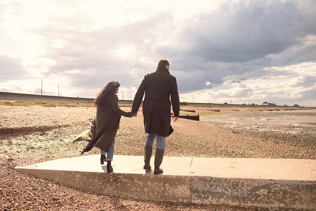 Couple in winter coats holding hands walking on sunny beach