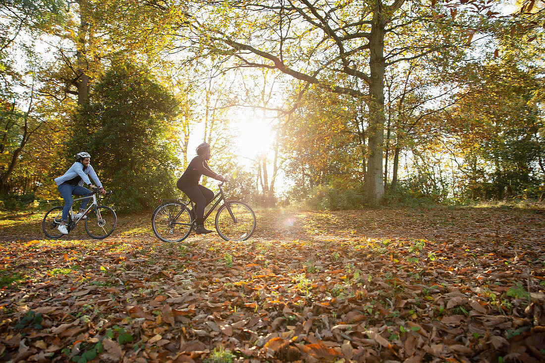 Couple riding bicycles in autumn leaves in sunny park
