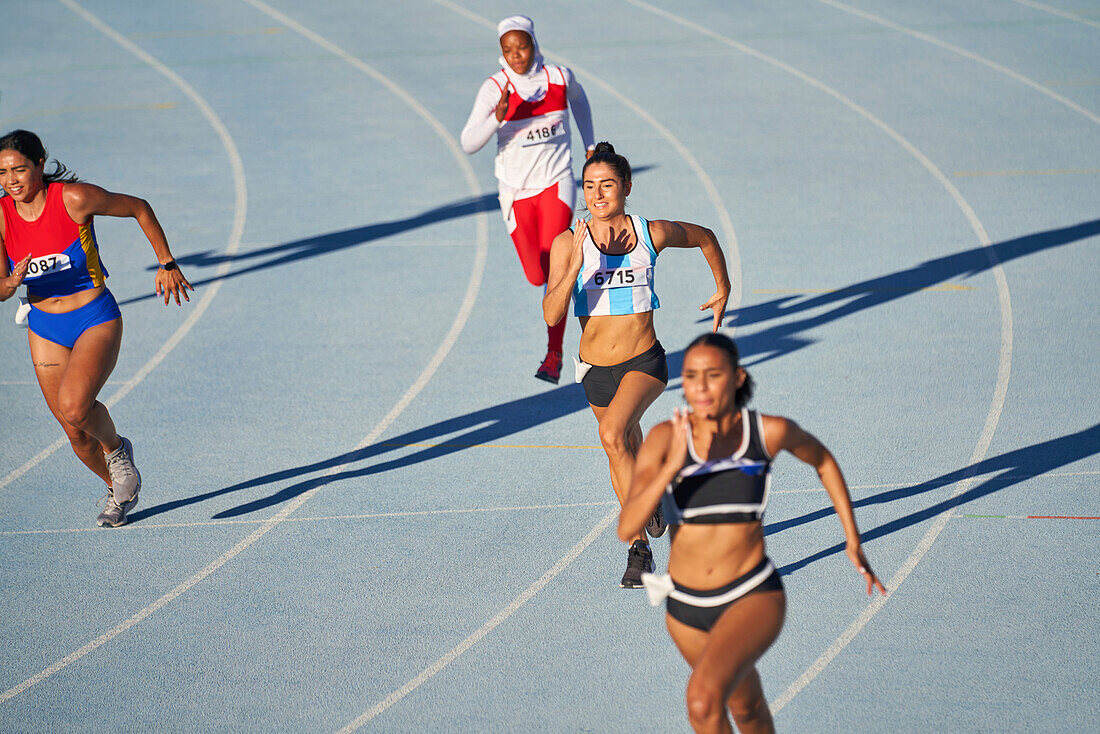 Female track and field athletes running on sunny blue track