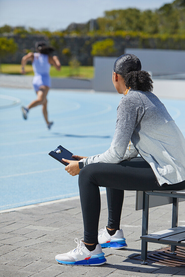 Female track and field coach watching runner on sunny track