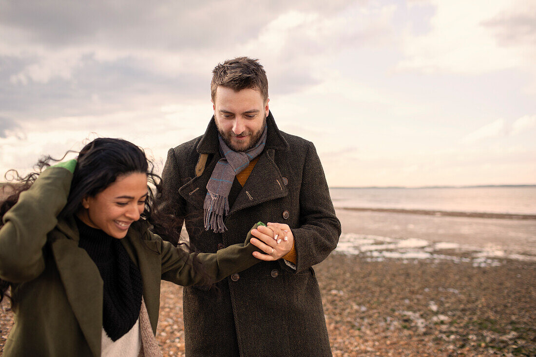 Happy couple in winter coats holding hands walking on beach