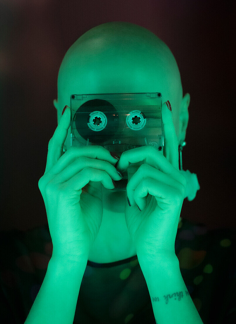 Woman with shaved head holding cassette tape in green light