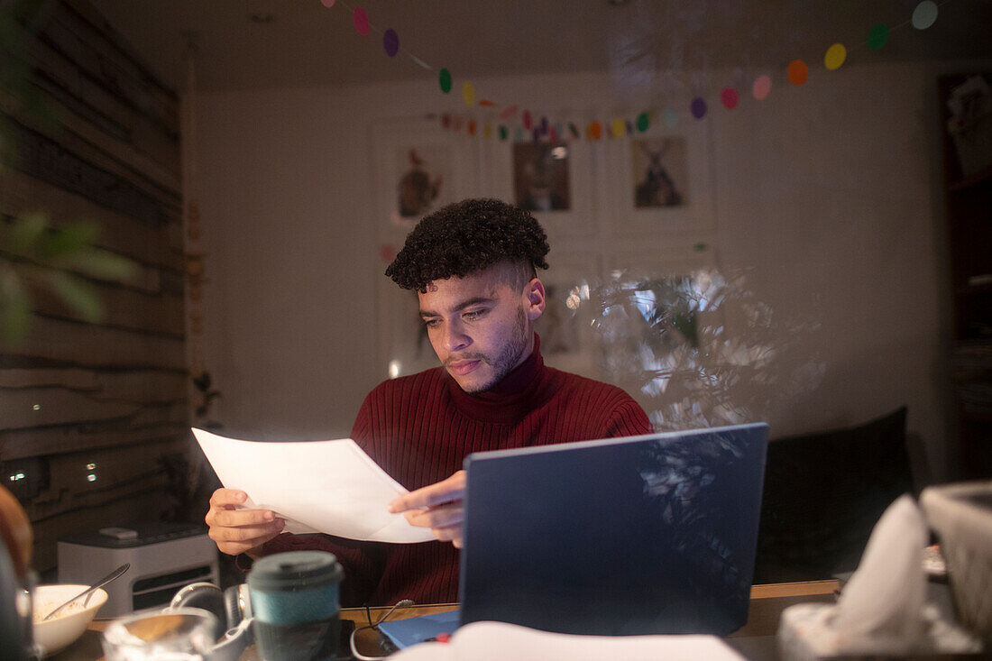 Focused young man with paperwork working late in home office