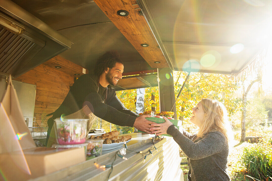 Happy food truck owner serving food to customer in park
