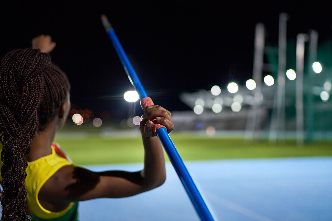 Female athlete throwing javelin in stadium at night