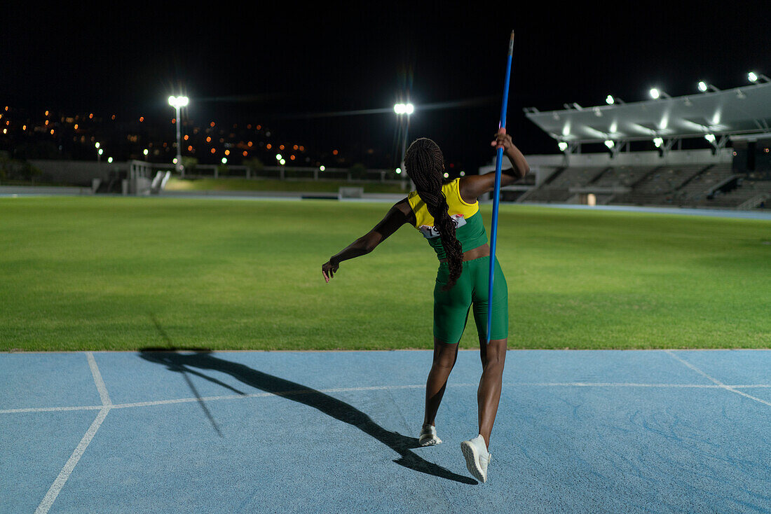 Female athlete throwing javelin in stadium at night