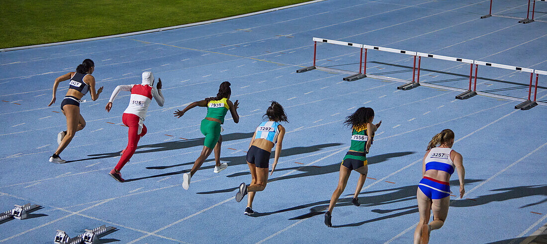 Female athletes racing toward hurdles in competition