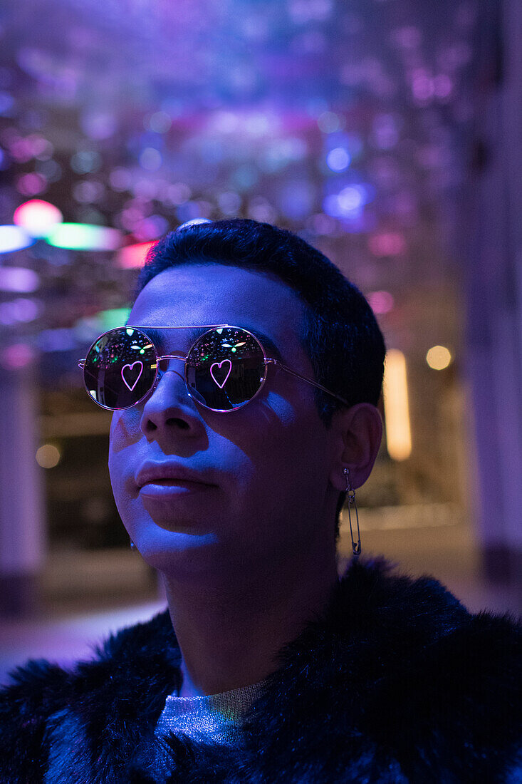 Reflection of neon heart in sunglasses of young man