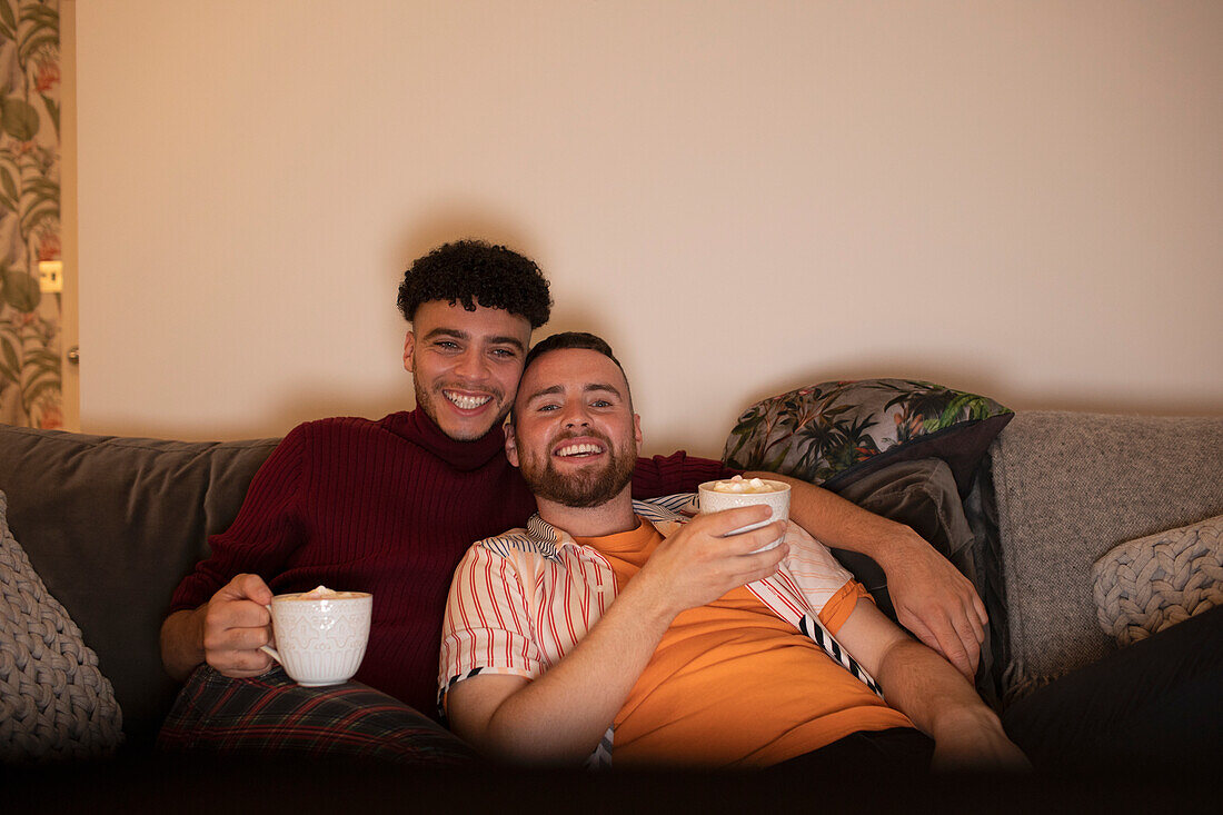 Happy affectionate gay couple with hot cocoa watching TV