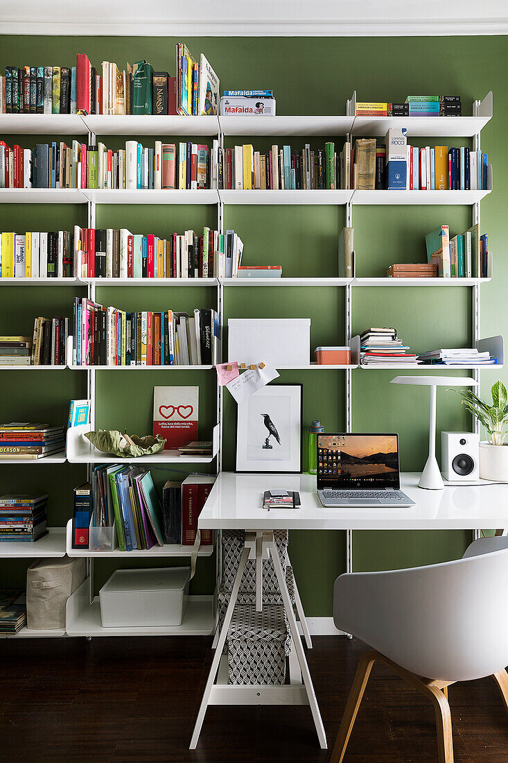 Weißer Schreibtisch, Schalenstuhl und Bücherregal im Arbeitszimmer mit grüne Wand