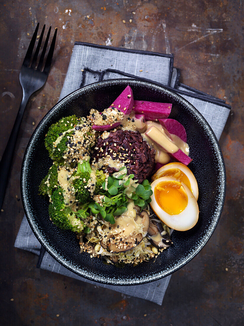 Vegetarian bowl with pickled eggs, broccoli, black rice, thahini sauce, sesamy seeds and mushrooms