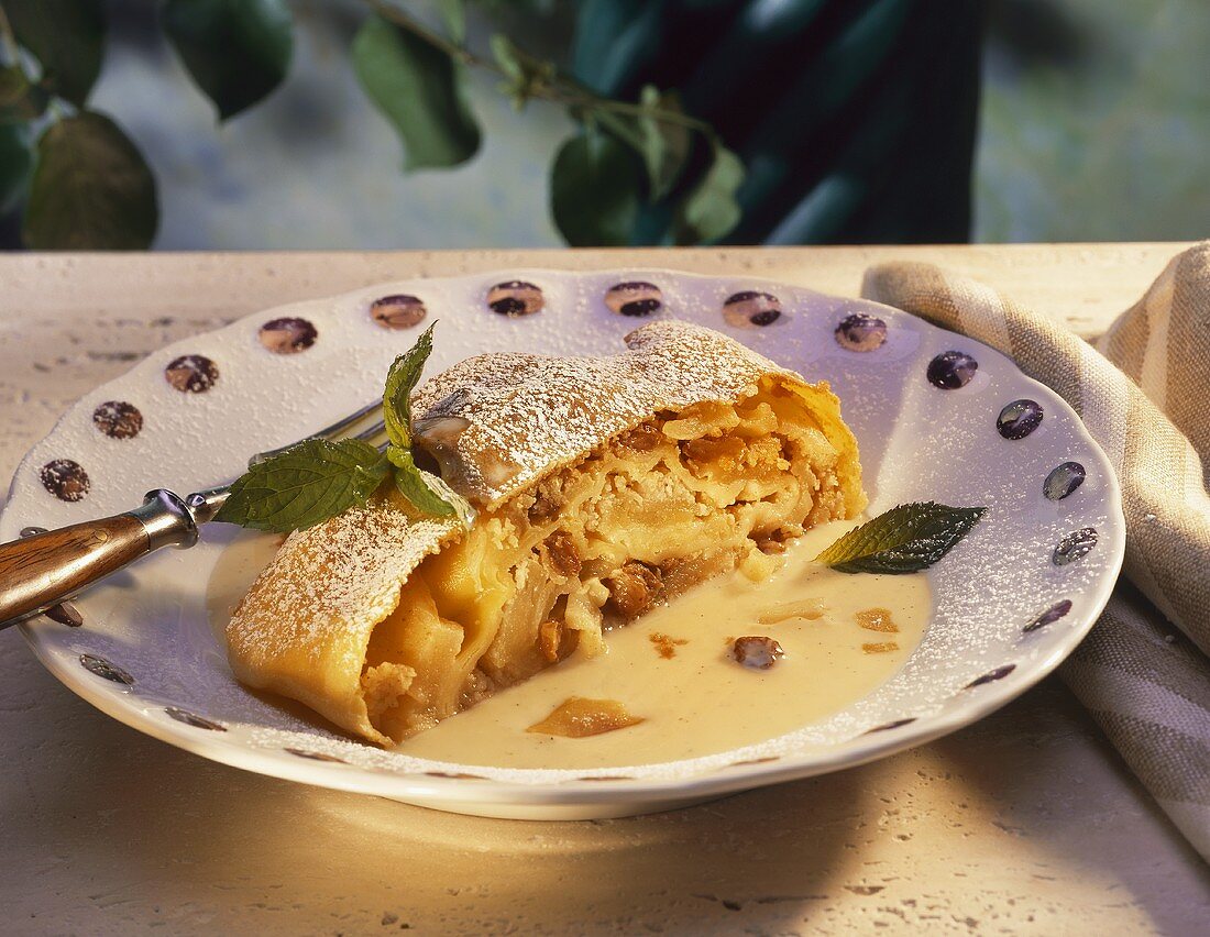 A piece of apple strudel with custard on plate