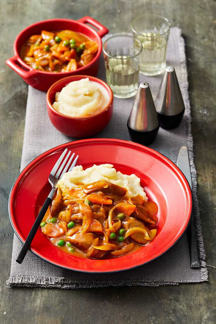 Wurst in Currysauce mit Erbsen und Karotten, dazu Kartoffelpüree