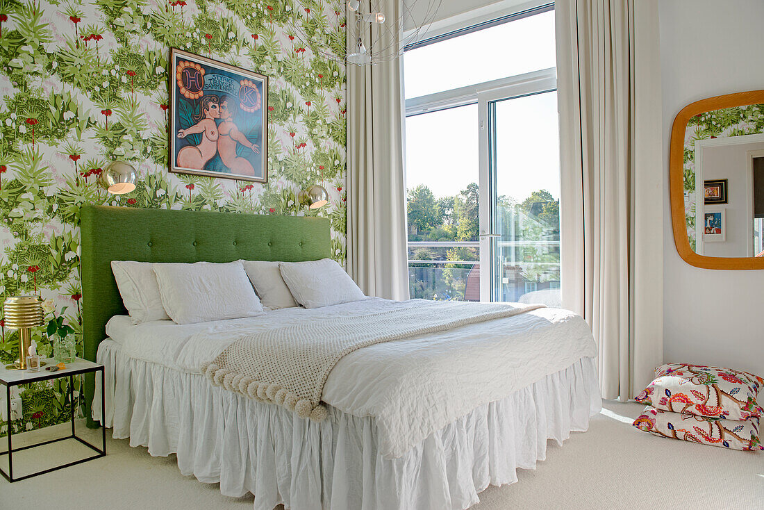 Double bed with green headboard in bedroom with floral wallpaper