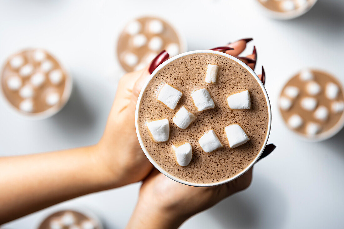 Hände halten eine Tasse heiße Schokolade mit Marshmallows