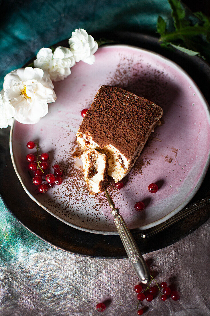 A piece of tiramisu garnished with currants and flowers