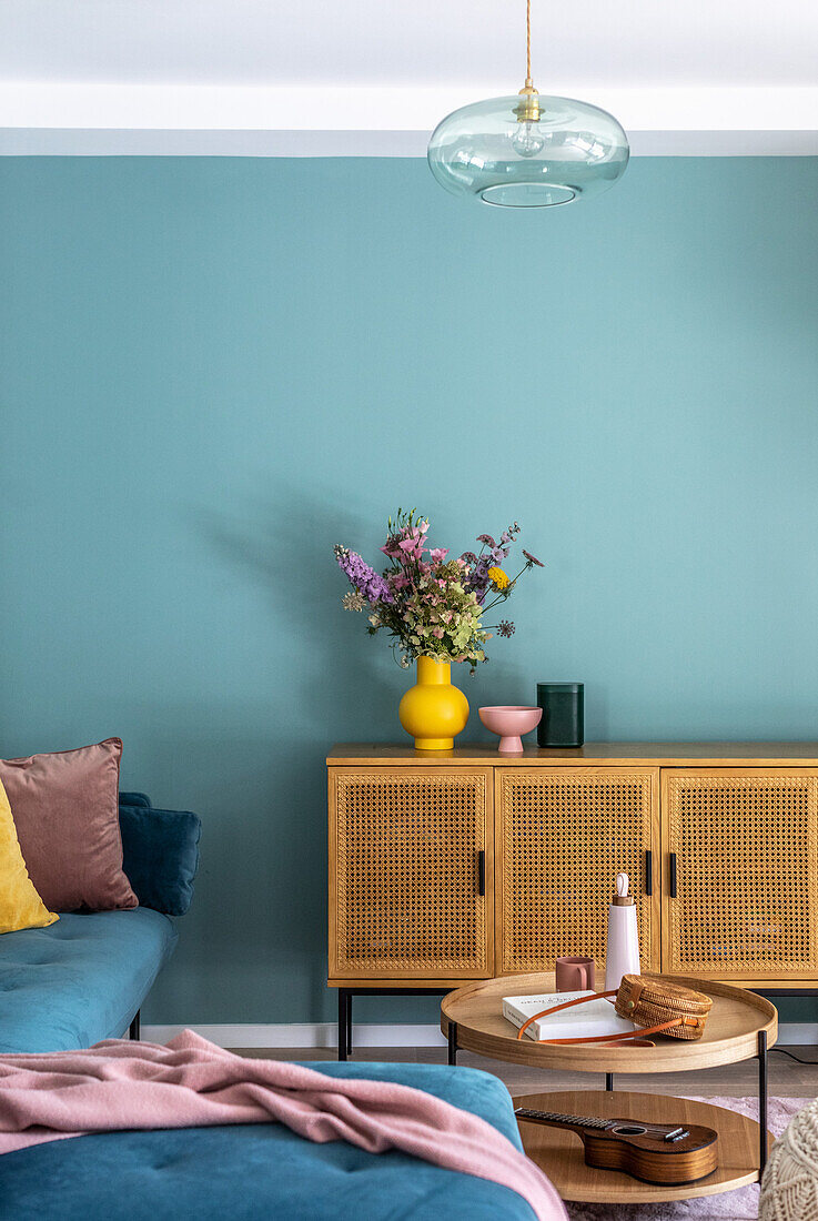 Ecksofa, Couchtisch und Lowboard mit Geflechttüren vor blauer Wand