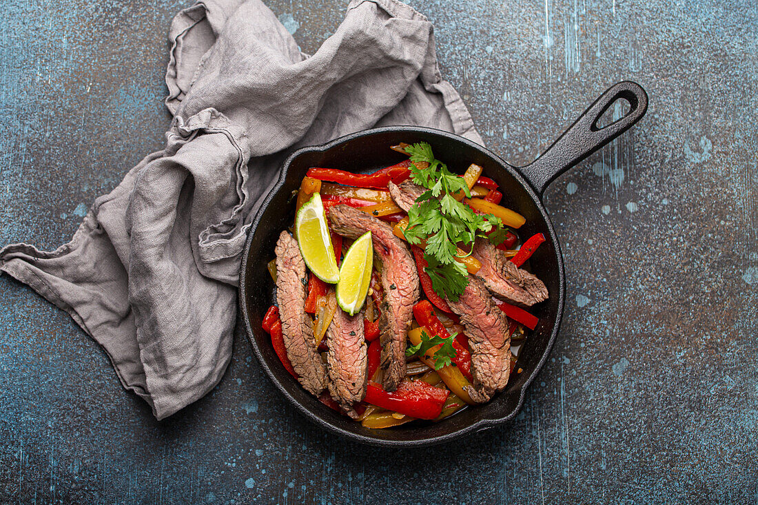 Beef fajitas with bell peppers in black cast iron pan