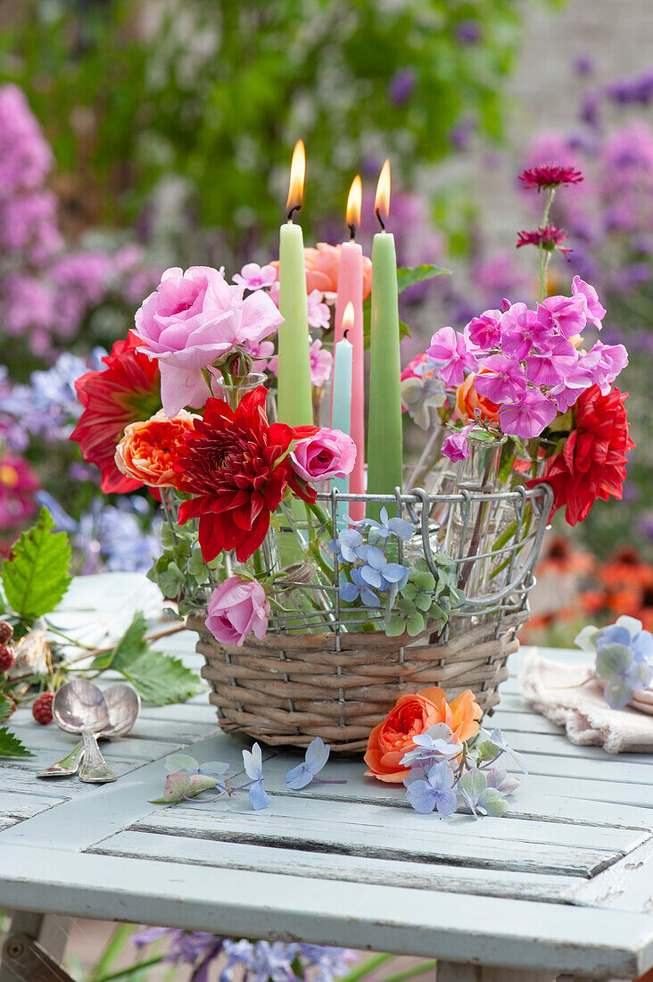 Basket with dahlia, rose, phlox and widow flower blossoms in bottles and candles as table decoration, rose blossom and hydrangea blossoms