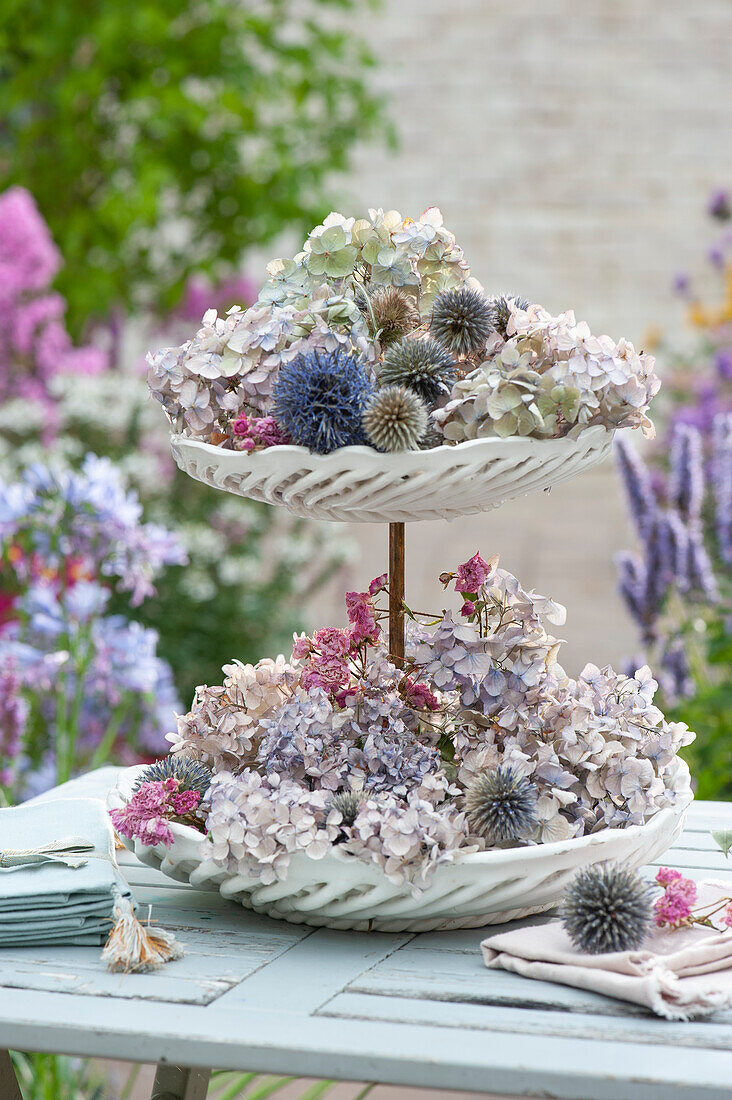 Etagere mit Hortensienblüten, Kugeldisteln und Miniröschen als Tischdeko