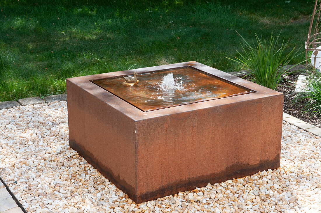 Square water feature made of Corten steel in a gravel bed